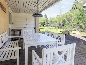 An outdoor patio with white wooden furniture, including a table and benches, under a covered area with a hanging light fixture. - 6 Person Holiday Home in Idestrup (Idestrup)