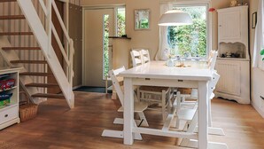 Een eetruimte met een witte tafel en stoelen, een hanglamp en een trap met houten treden.
