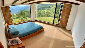 A bedroom with a large bed, two windows, and a view of a mountainous landscape. - TCFR - Stay in a UNESCO Biosphere Reserve - Nature, Comfort, and Adventure! (Quito)