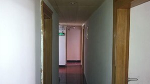 Een smalle gang met houten deuren aan weerszijden, die leidt naar een kamer met een rode vloerbedekking.