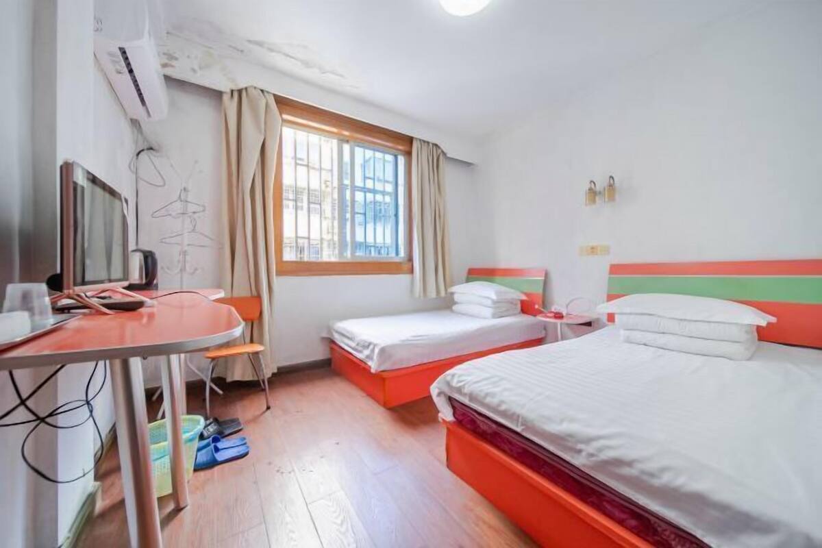 A hotel room with two beds, a desk, a chair, a TV, and a window with curtains.
