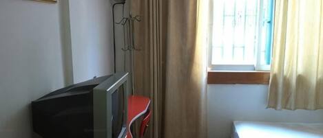 A room with a bed, a television on a red stand, an air conditioning unit, and a window with curtains.