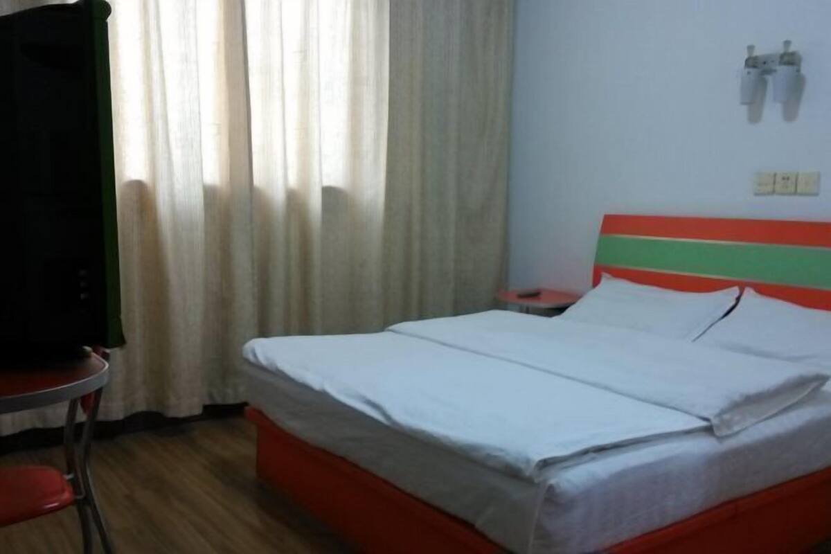 A hotel room with a bed, a nightstand, a TV, and a window with curtains.