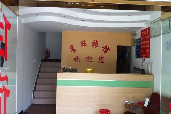 A reception area with a wooden reception desk, a staircase, and a wall with red text. - Xingwang Hostel (Shanghai)