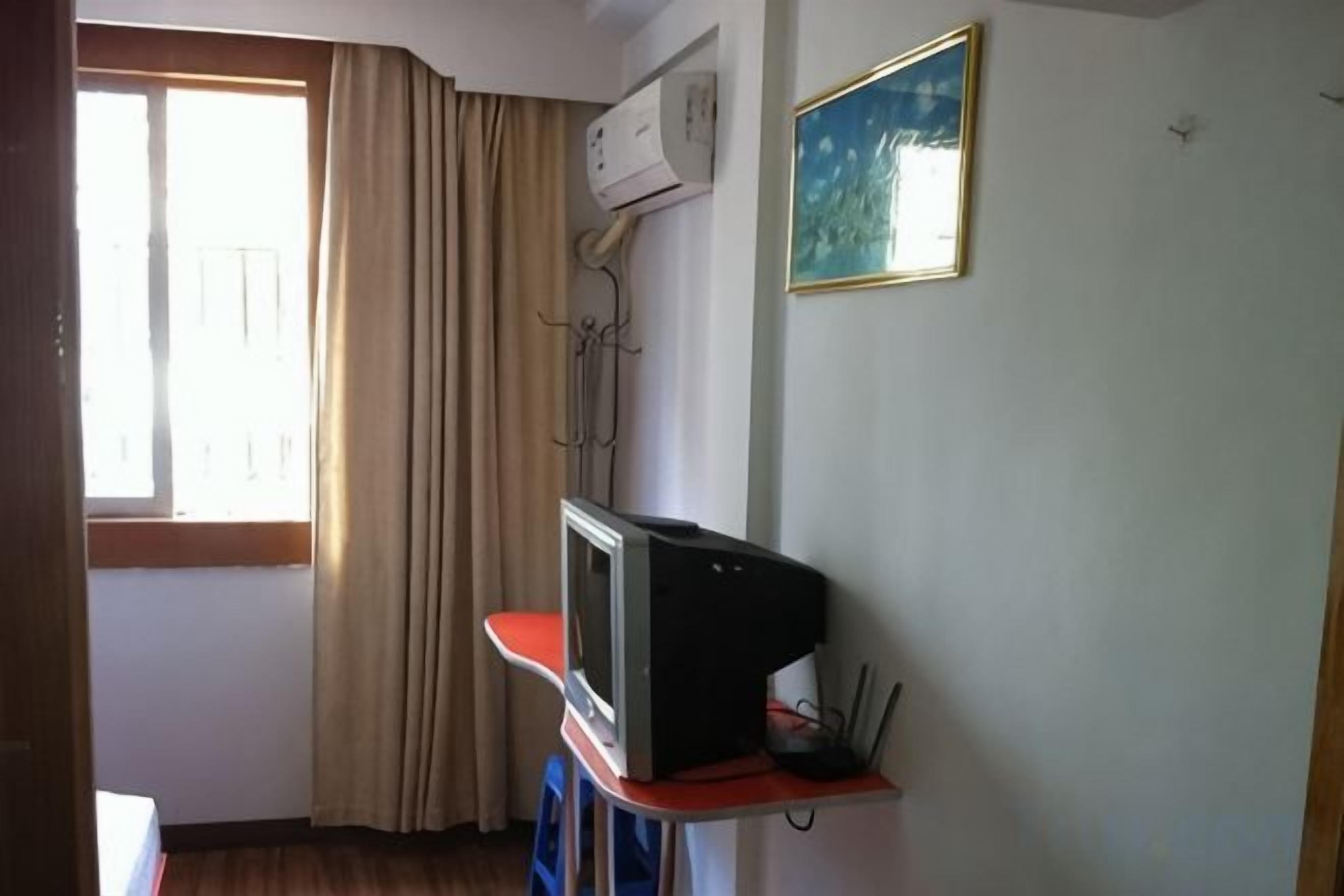 A room with a television on a stand, a window with curtains, and an air conditioning unit on the wall.
