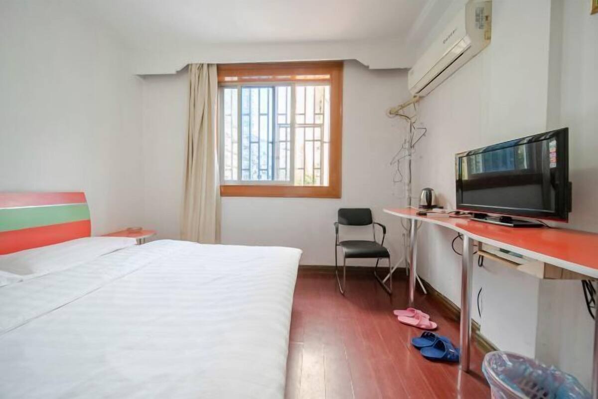 A hotel room with a bed, a desk with a television, a chair, and a window with curtains.
