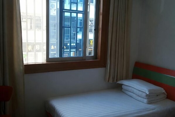 Un lit simple avec un matelas à rayures et une couverture blanche soigneusement pliée.