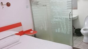 Een hotelkamer met een bed, een tafeltje, een douchecabine van glas, een wastafel en een toilet.