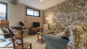 Una sala de estar acogedora con pared de piedra, un televisor, una mesa de madera y un sofá.