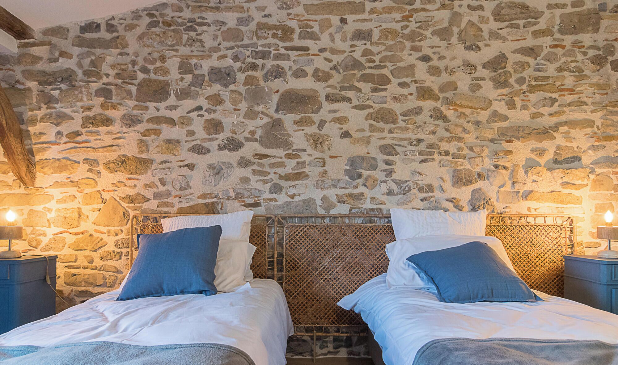 Quarto com duas camas, paredes de pedra e vigas de madeira.