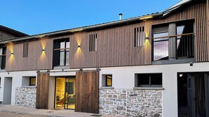 Un edificio moderno con fachada de piedra, grandes puertas de madera y un balcón con barandillas.