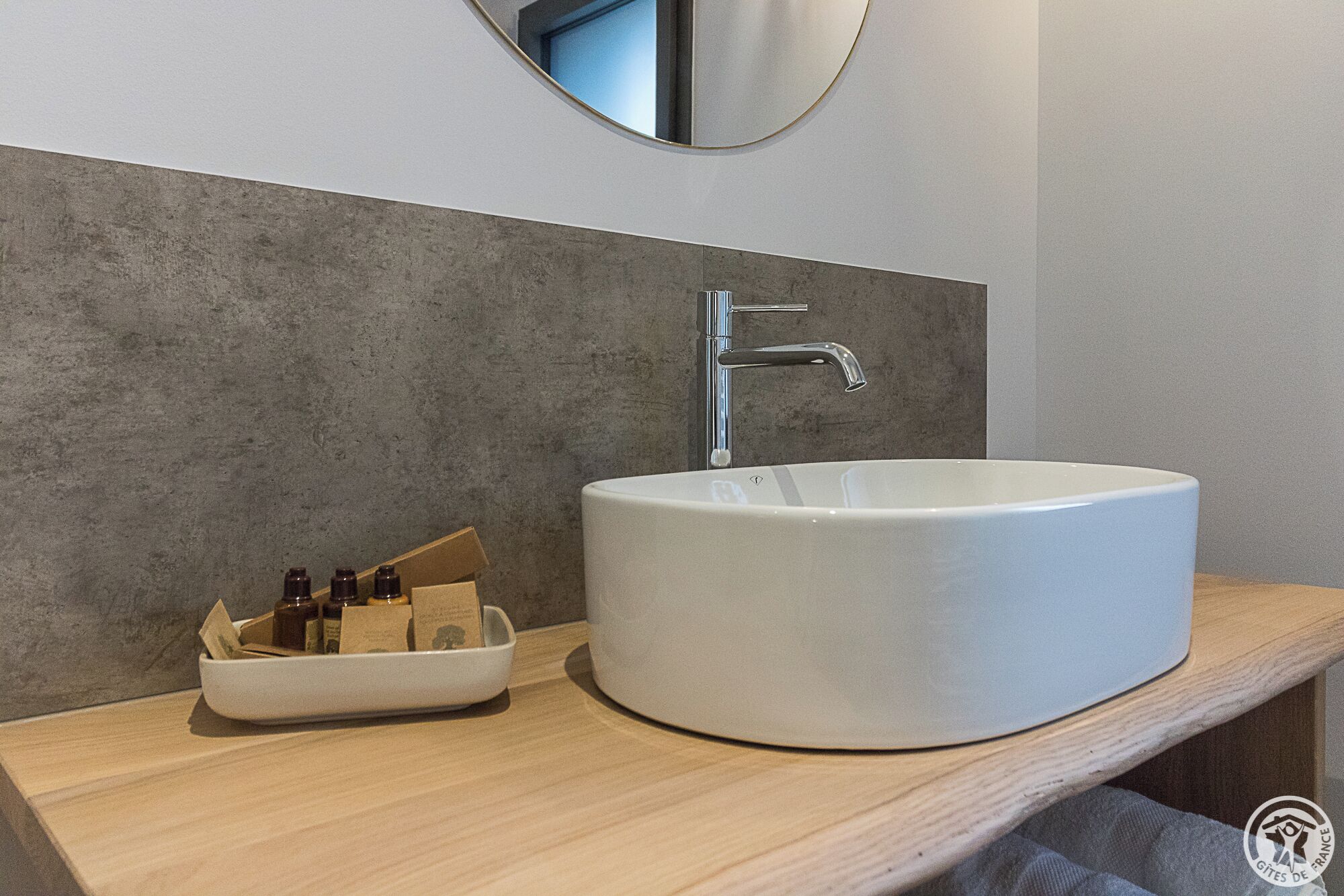 A modern bathroom with a round white sink, a chrome faucet, and a wooden countertop.