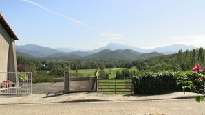 Vista de un paisaje rural con montañas a lo lejos, una entrada con portón y un edificio con techo rojo.