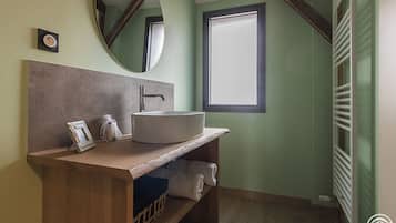 Un bany amb un penjador de fusta, un lavabo rodó, un mirall i una finestra.