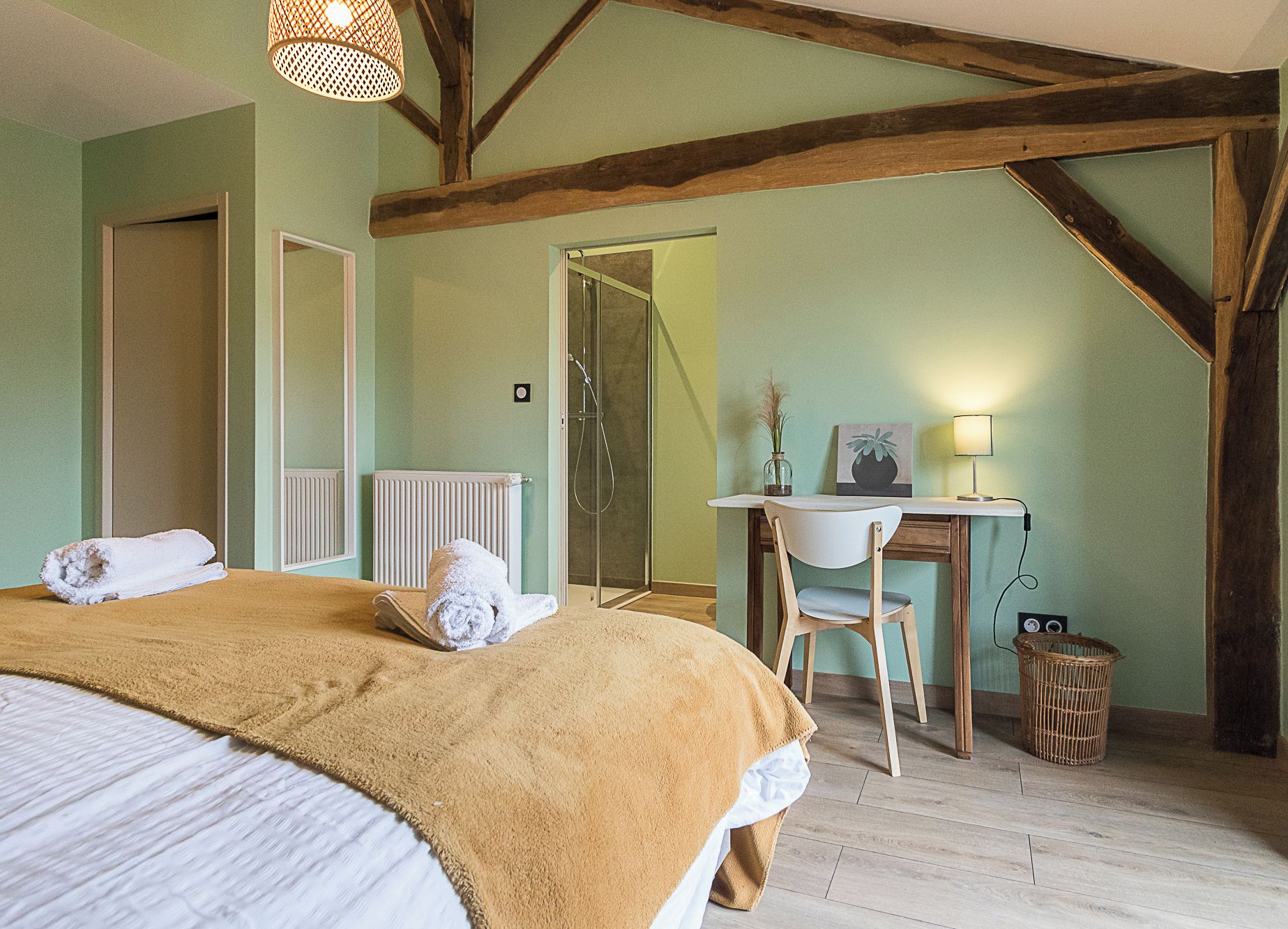 A bedroom with a bed, a desk, and a chair. There is a radiator, a window, and a door.