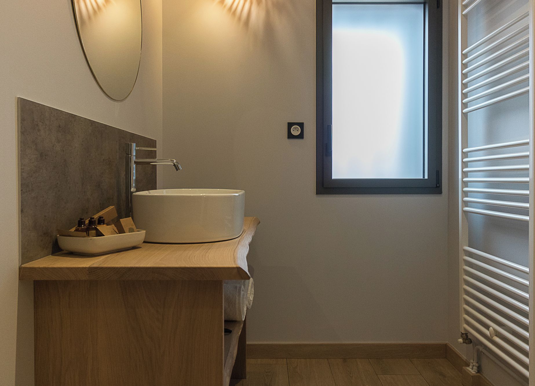 Une salle de bain moderne avec un lavabo rond, un meuble-lavabo en bois, un miroir, une fenêtre et un radiateur.