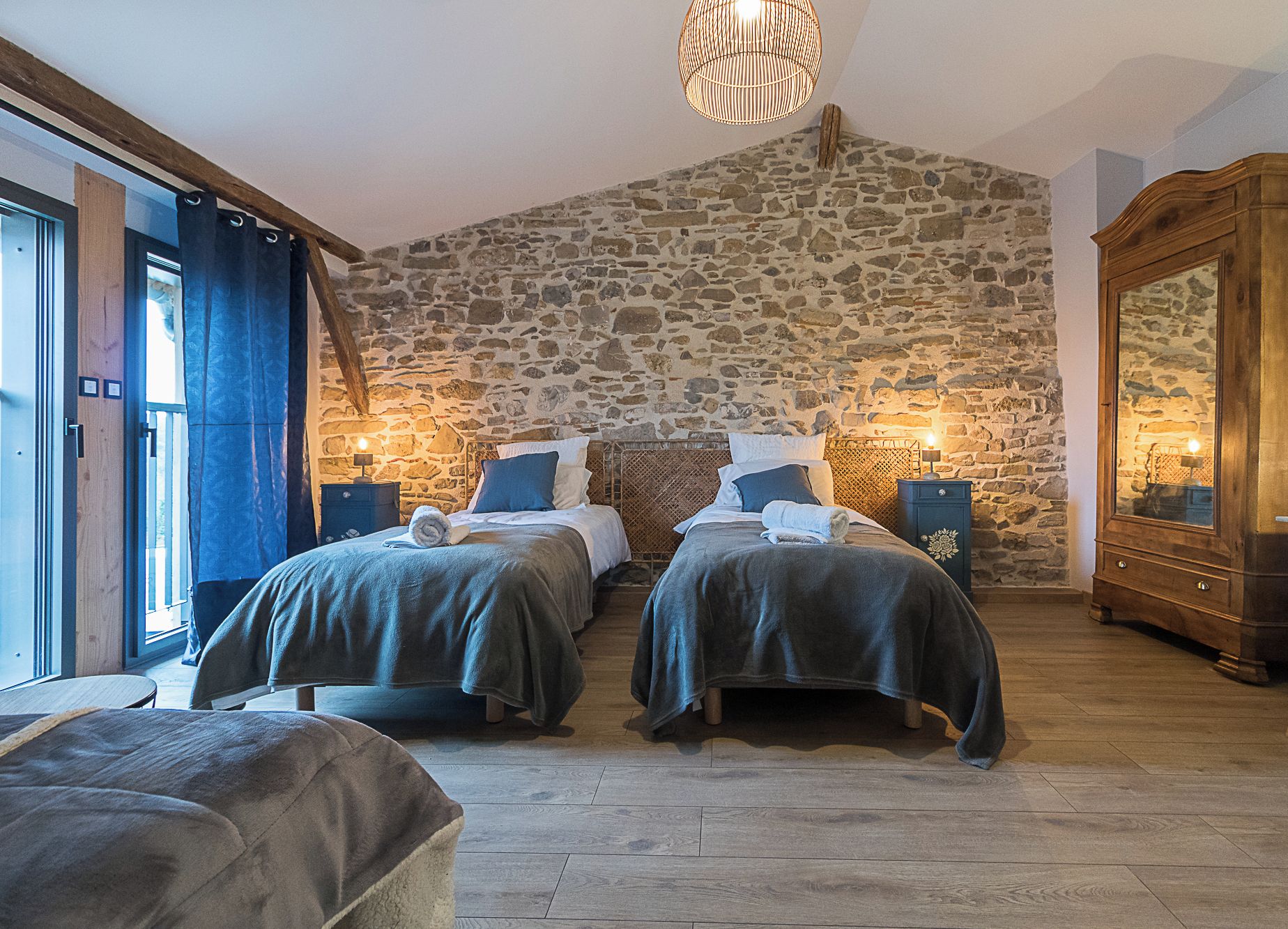 Ein Zimmer mit zwei Betten, Steinwänden, Holzmöbeln und einer Chandelier.