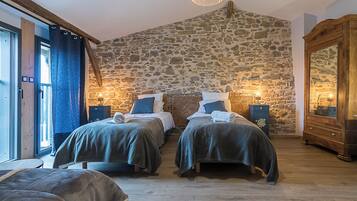 Ein Zimmer mit zwei Betten, Steinwänden, Holzmöbeln und einer Chandelier.
