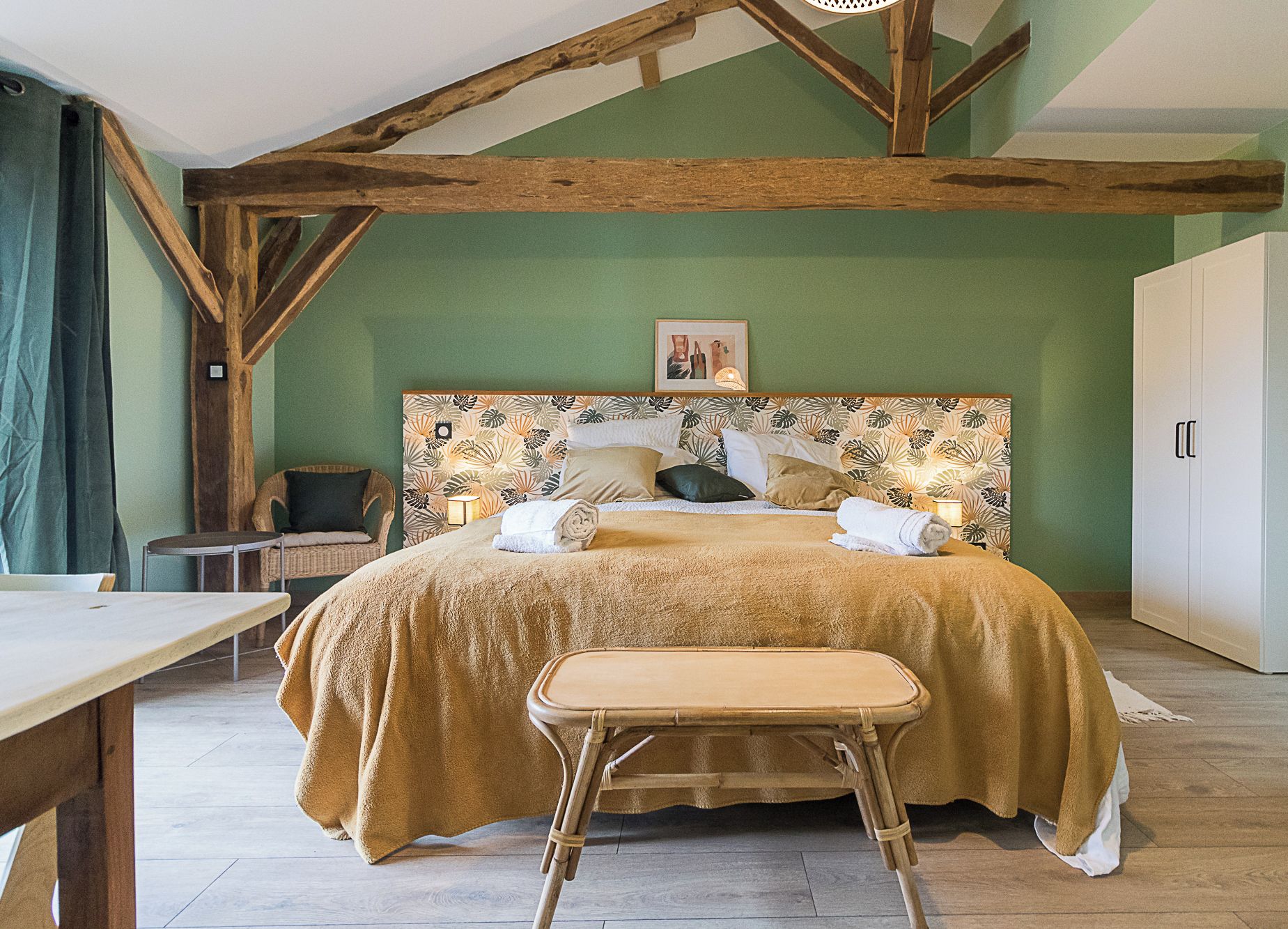 Une chambre à coucher avec un grand lit, une tête de lit en bois, un petit tabouret, une chaise et une armoire.