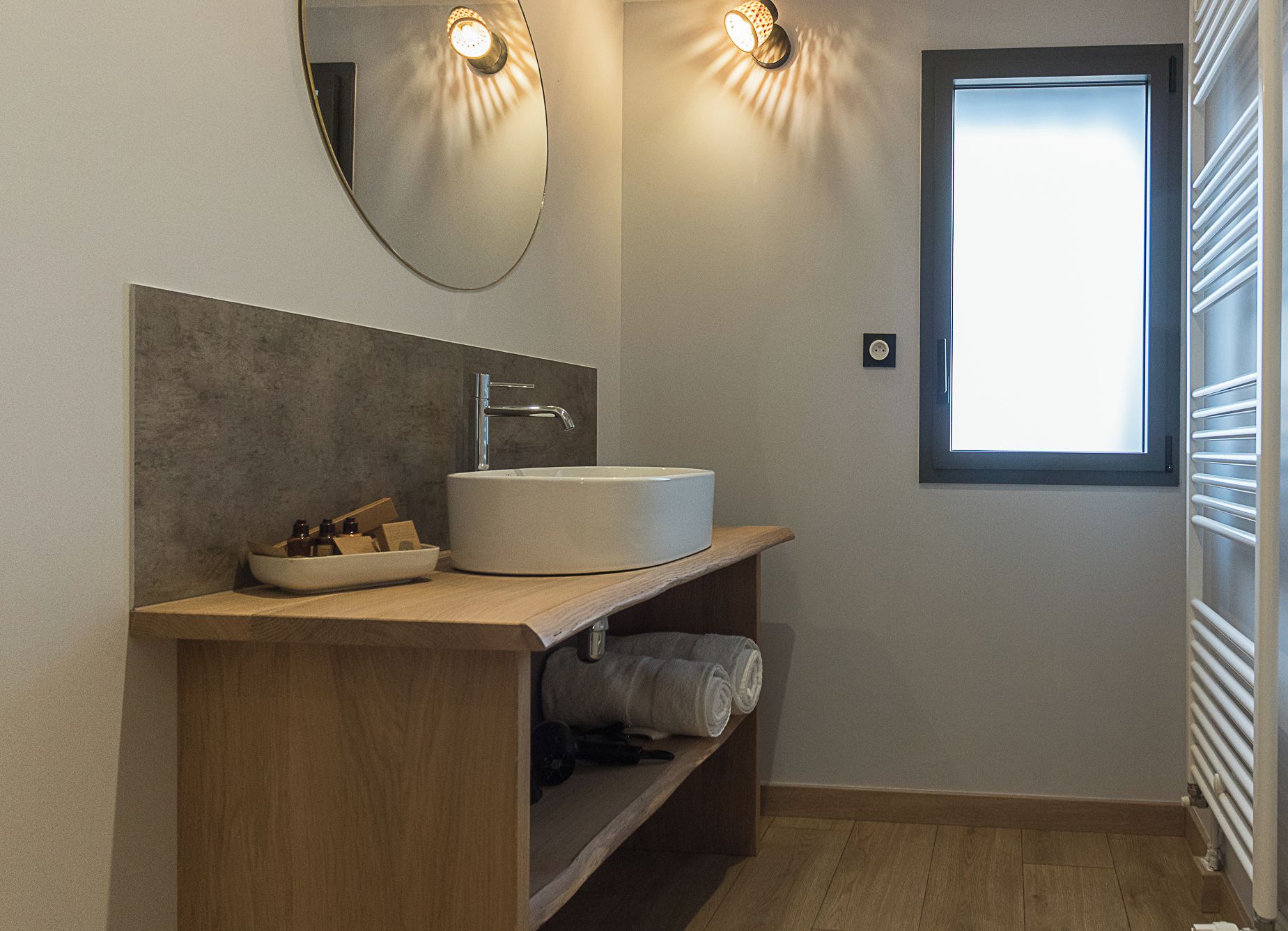 Une salle de bain moderne avec un lavabo rond, un meuble-lavabo en bois et une fenêtre laissant entrer la lumière naturelle.