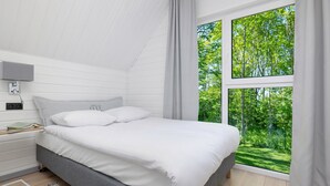 A bedroom with a bed, a nightstand, a lamp, and a window with a view of greenery. - Ferienhaus in Meernahe, Trzesacz (Rewal)