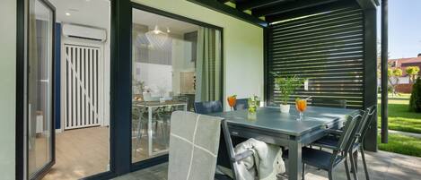 Un espace extérieur aménagé pour les repas, avec une table et des chaises, une terrasse couverte et une vue sur la cuisine adjacente.