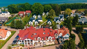 An aerial view of a coastal residential area with houses, a large central building with a red roof, and a body of water in the background. - Ferienhaus in Meernahe, Trzesacz (Rewal)