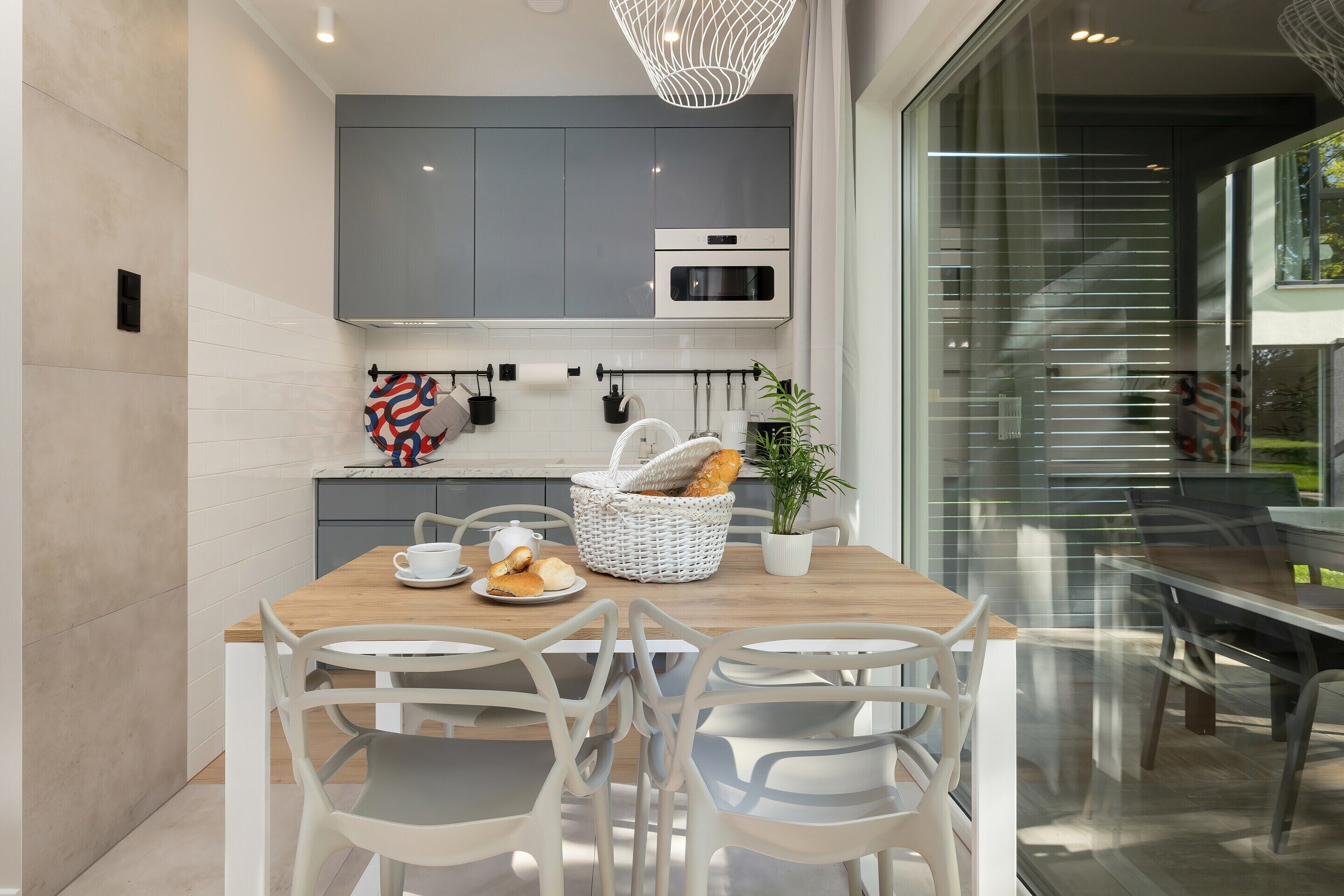 A modern kitchen with grey cabinets, a wooden dining table, and white chairs.