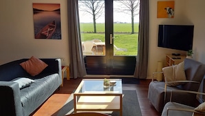 Een woonkamer met een bank, fauteuil, salontafel en een tv op een standaard.