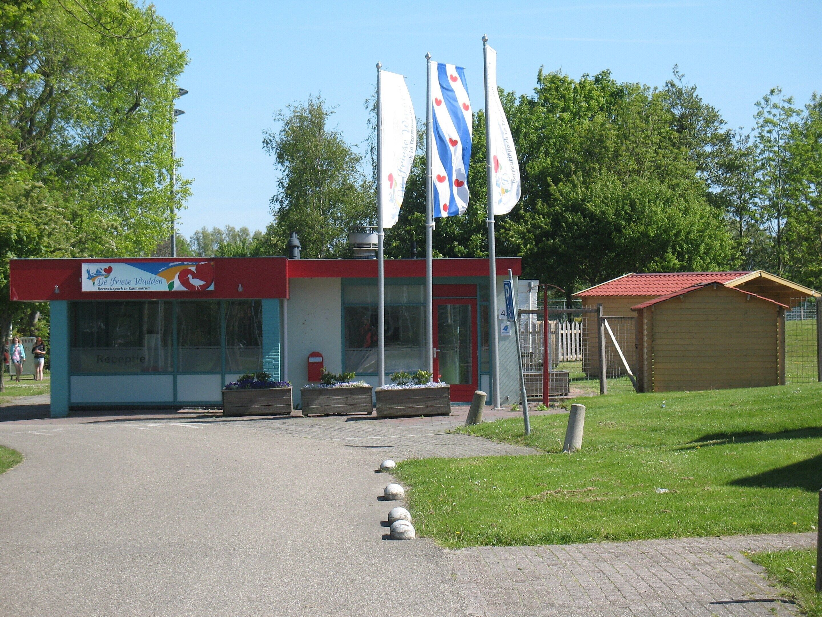 A small building with a red roof and a sign that reads "Recreatiepark in Tammarum." There are three flags on flagpoles in front of the building.