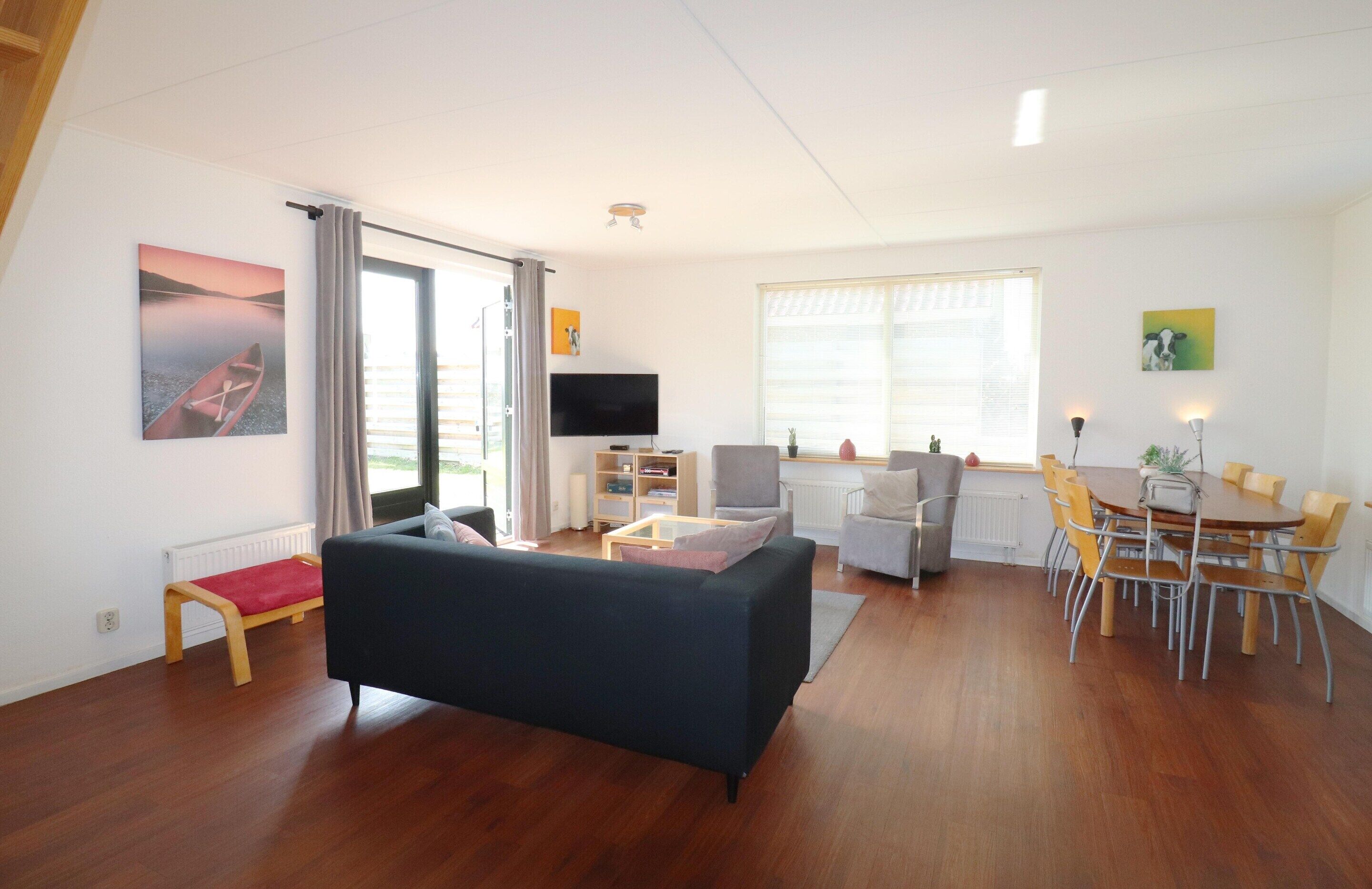 A modern living room with a sofa, a dining table with chairs, a TV, and a bookshelf.