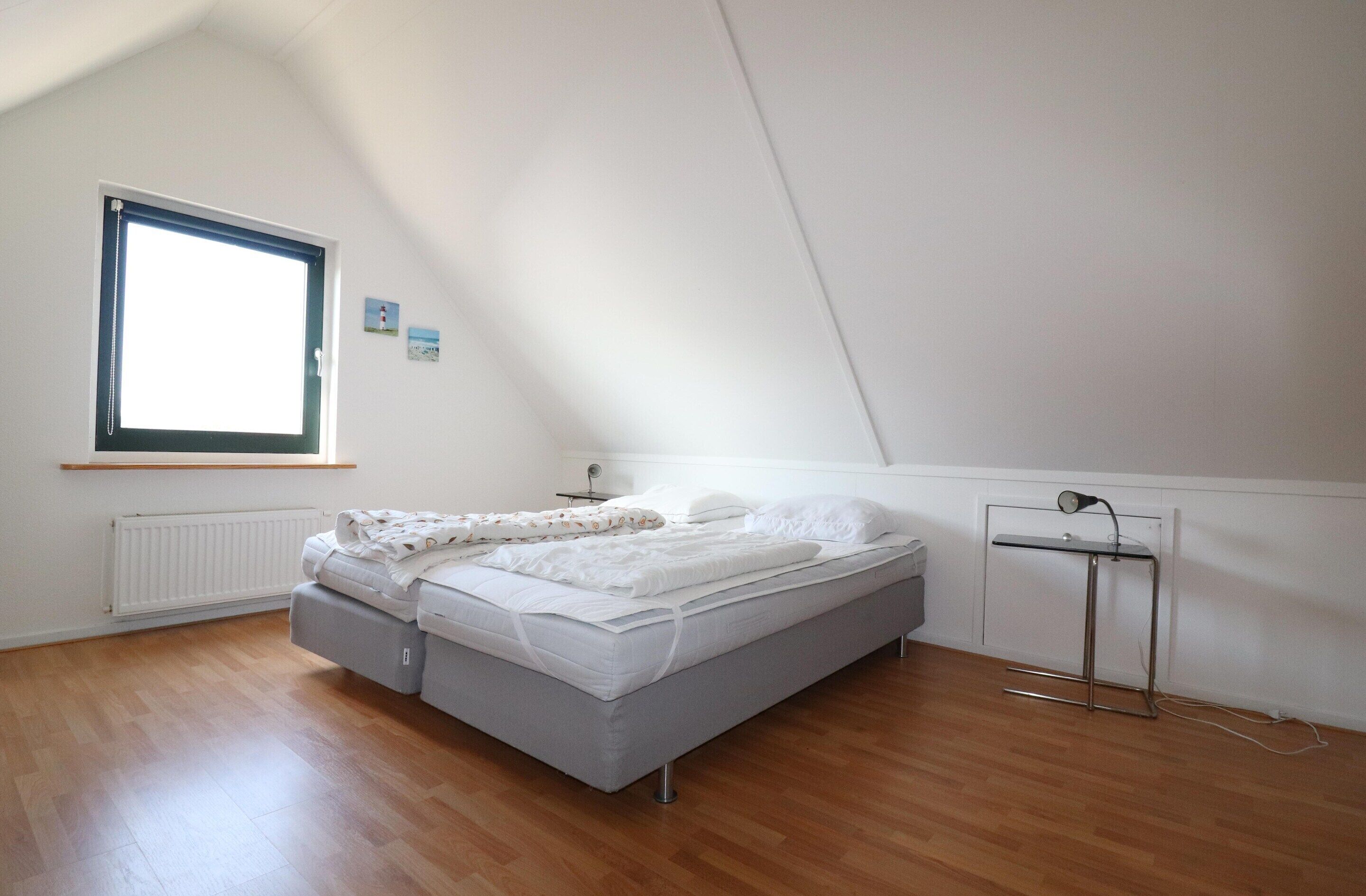 Une chambre à coucher avec un lit, une fenêtre, un radiateur et une petite table avec une lampe.
