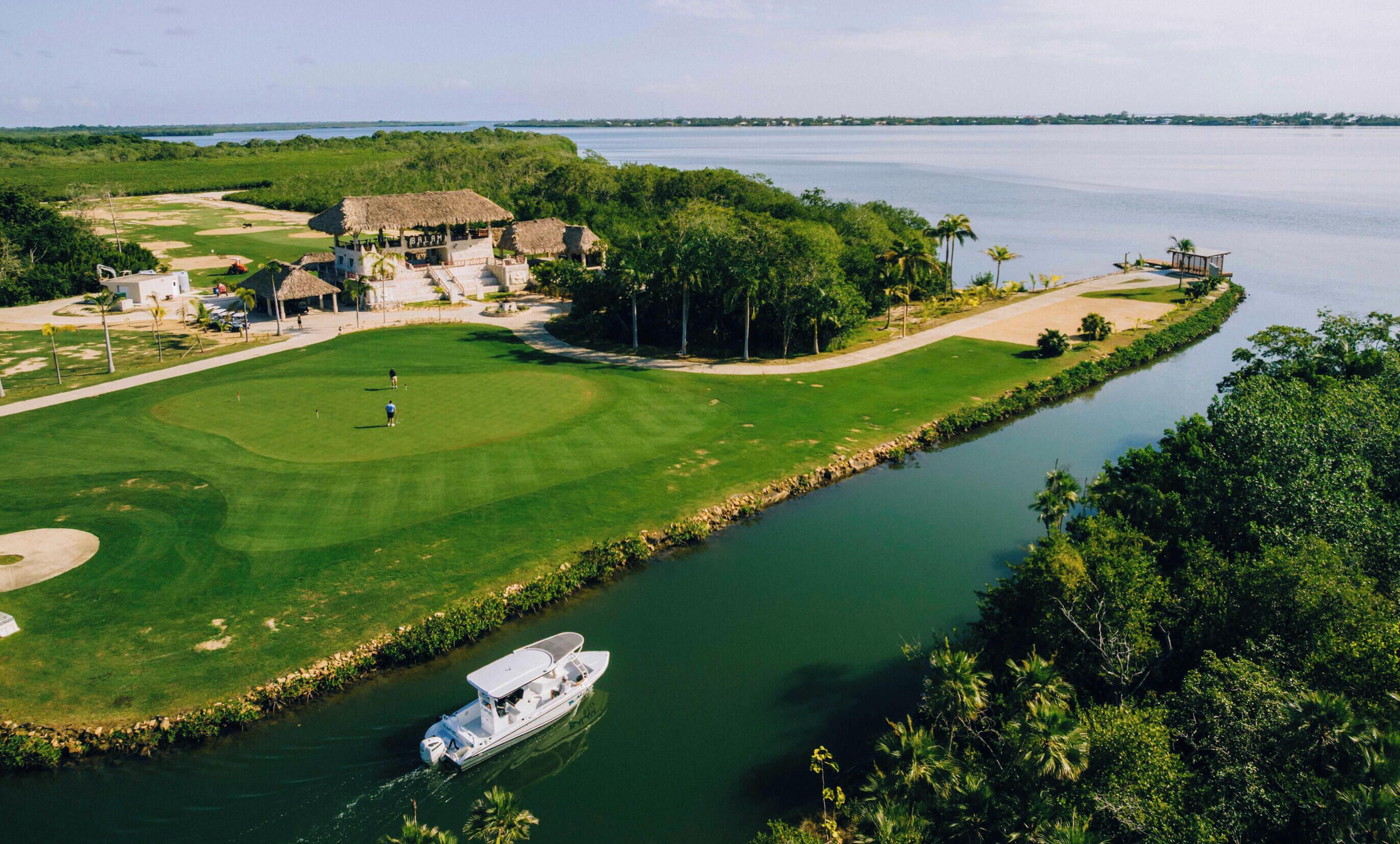 A golf course with a water body, a boat, and a building with a thatched roof.