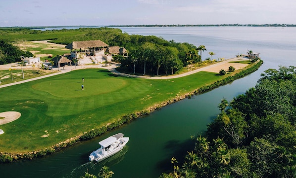 Un campo de golf con un cuerpo de agua, un bote y un edificio con techo de paja.
