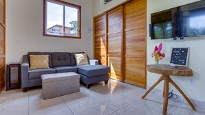 Una sala de estar con un sofá seccional gris, un pequeño reposapiés, un aparador de madera, un televisor de pantalla plana y un letrero de bienvenida.
