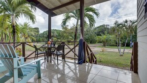 Un patio cubierto con una mesa y sillas, rodeado de palmeras y vistas al jardín.