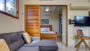 Una sala de estar moderna con un sofá seccional gris, una cama de madera con ventilador de techo y un televisor sobre un mueble de madera.
