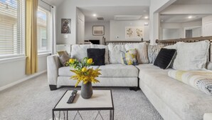 A modern living room with a grey sofa, a coffee table with a vase, and a remote control. - Luxury 4BRS-3Baths Home, w/ King Bed & Private Gym (Katy)