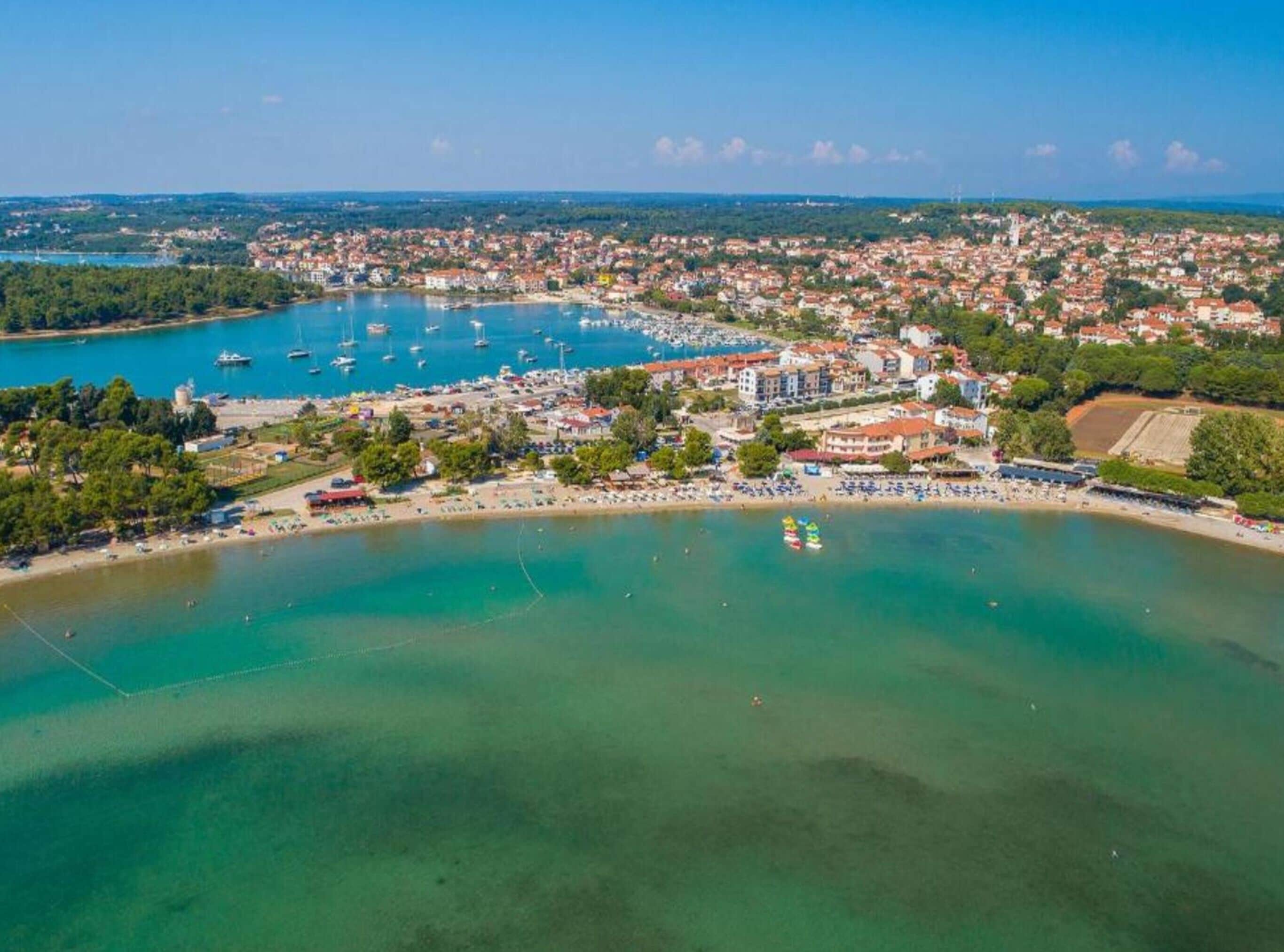 Vue aérienne d’une ville côtière avec un port de plaisance, des plages de sable et des immeubles d’habitation.