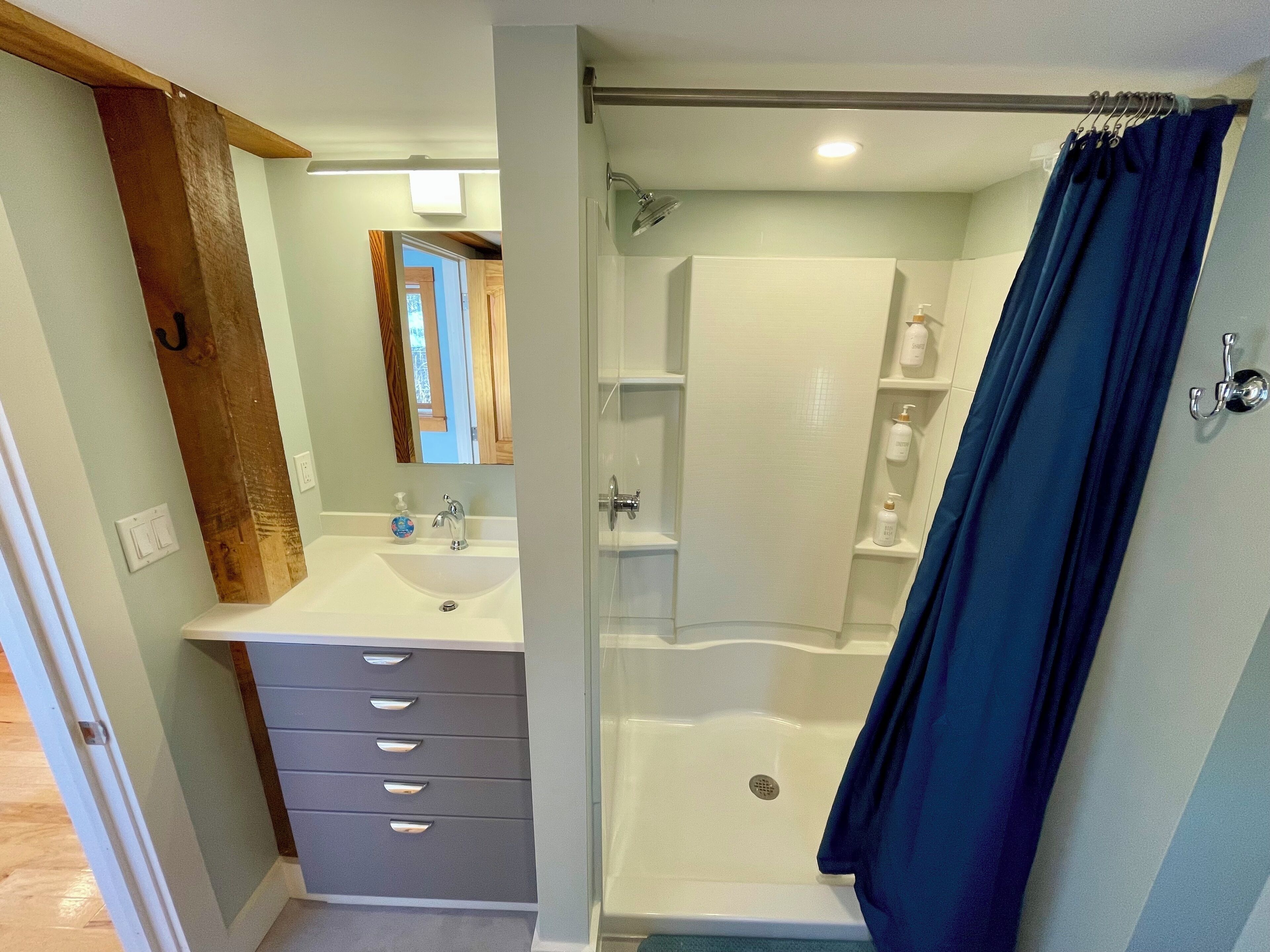 A bathroom with a white sink, a mirror, a shower, and a blue shower curtain.