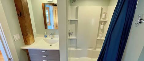 A bathroom with a white sink, a mirror, a shower, and a blue shower curtain.