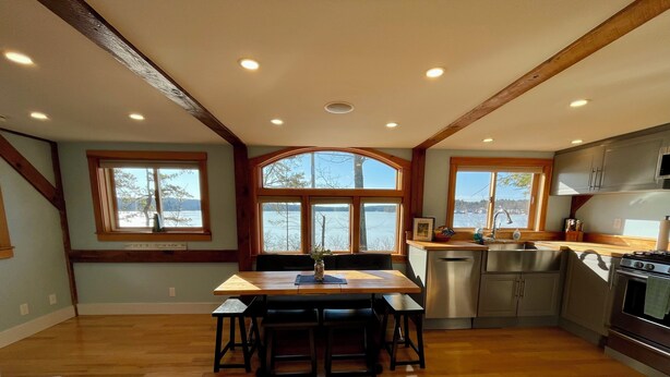 Une cuisine spacieuse avec un plancher en bois, un coin repas avec une table et des chaises, et de grandes fenêtres offrant une vue sur un lac.