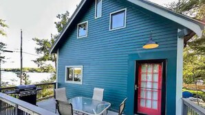 Une maison bleue avec une porte rouge, un balcon avec une table et des chaises, et un luminaire suspendu.