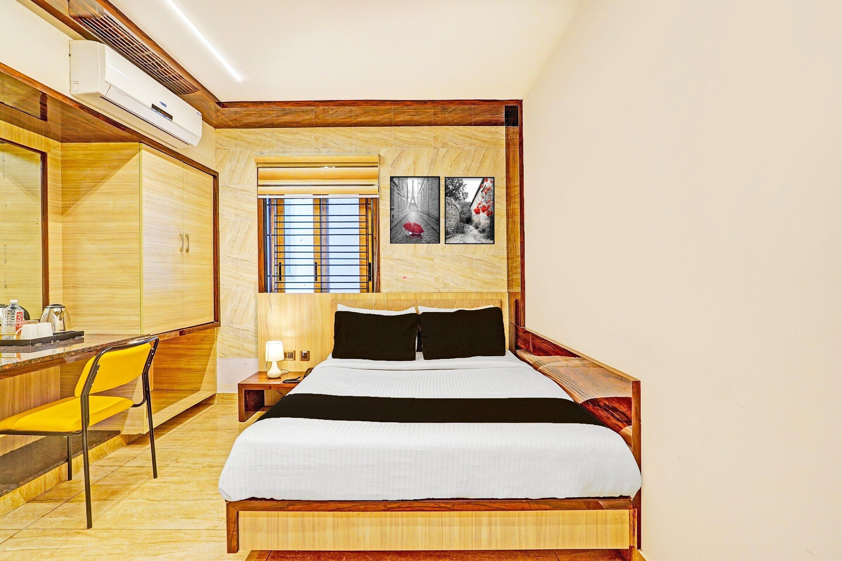 Ein Hotelzimmer mit einem Holzbett, einem Schreibtisch mit Stuhl, einem Fenster mit Jalousien und einer Wand-Klimaanlage.