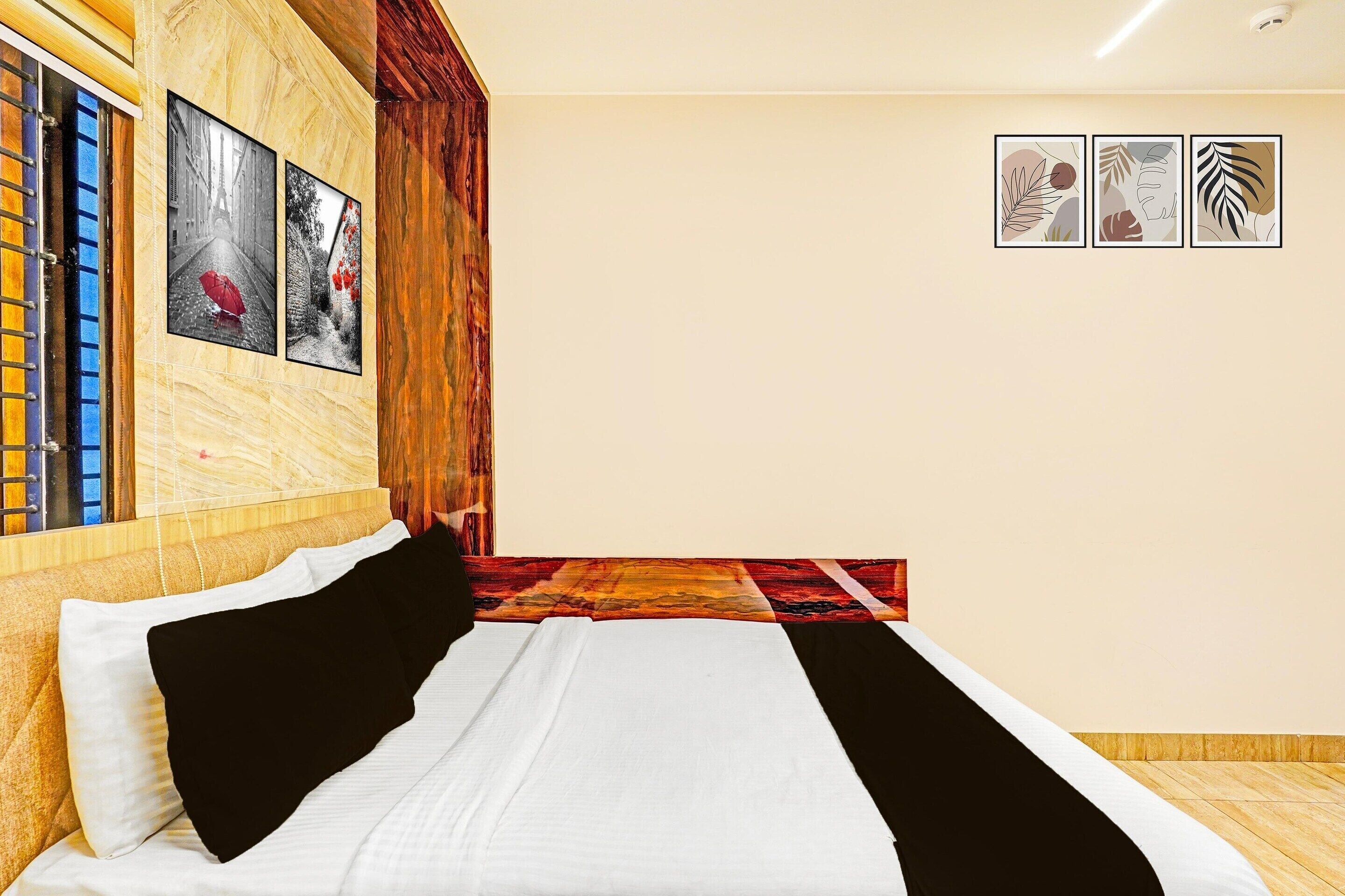 Une chambre d’hôtel avec un lit, une tête de lit en bois, une fenêtre avec des stores et trois tableaux encadrés accrochés au mur.