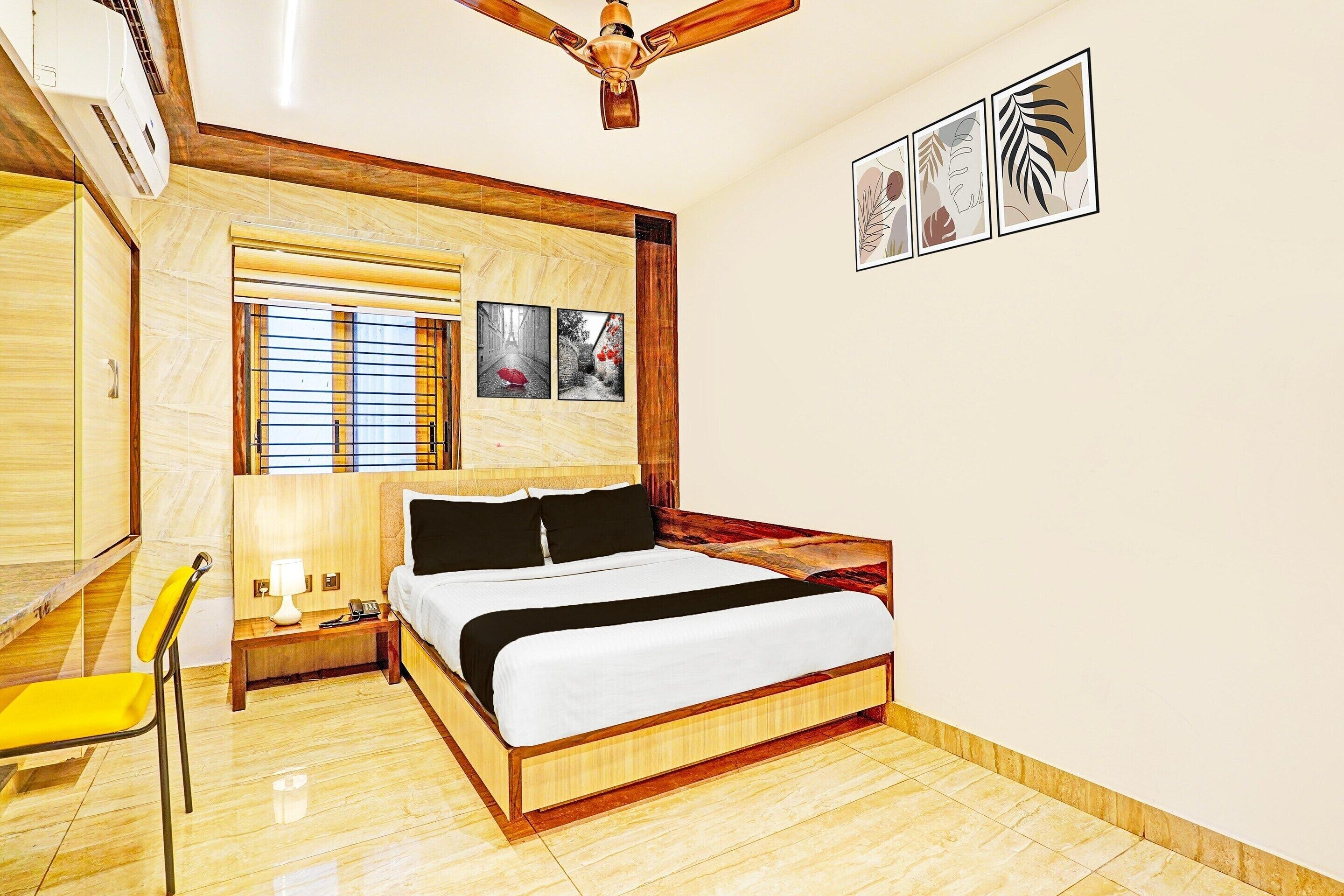 A modern hotel room with a wooden bed, a desk with a chair, a window with blinds, and artwork on the wall.