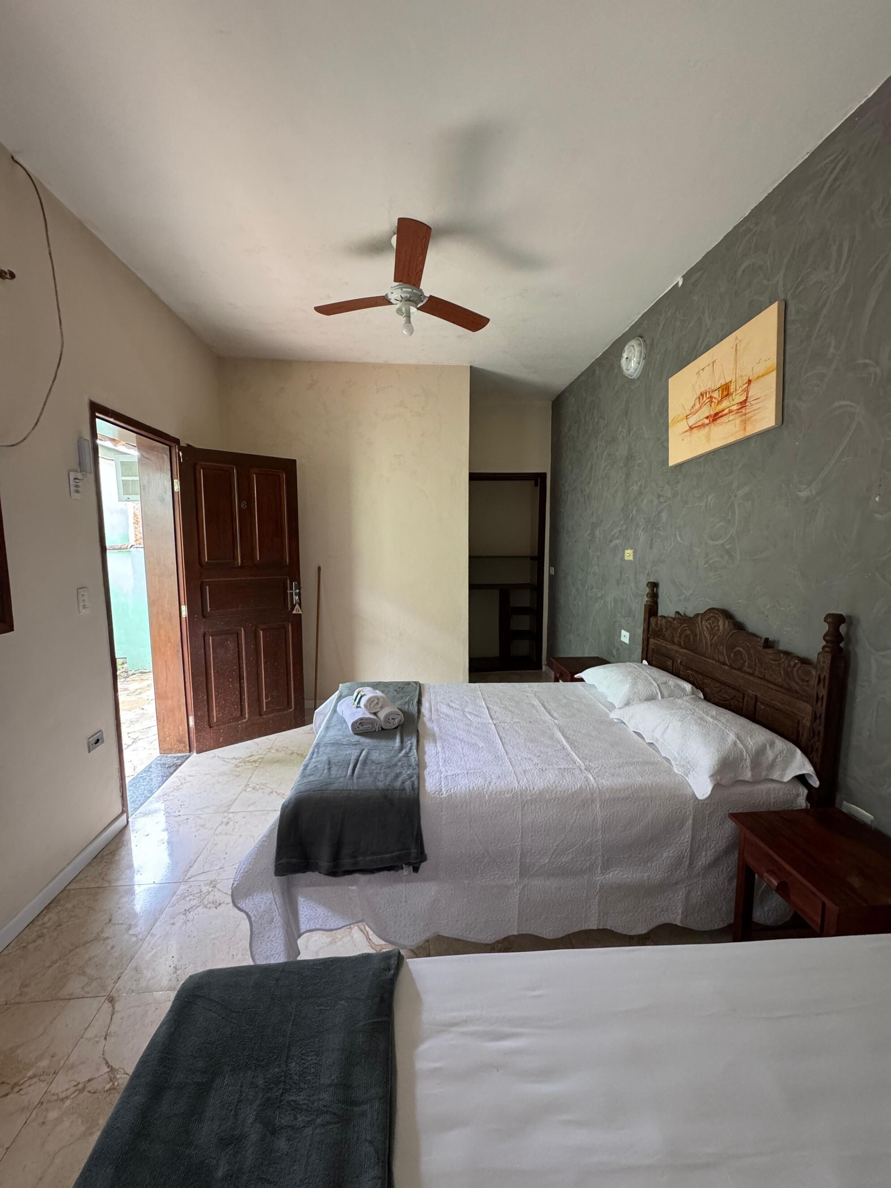 Un dormitorio con dos camas, un ventilador de techo, un cuadro en la pared y una puerta que da a otra habitación.