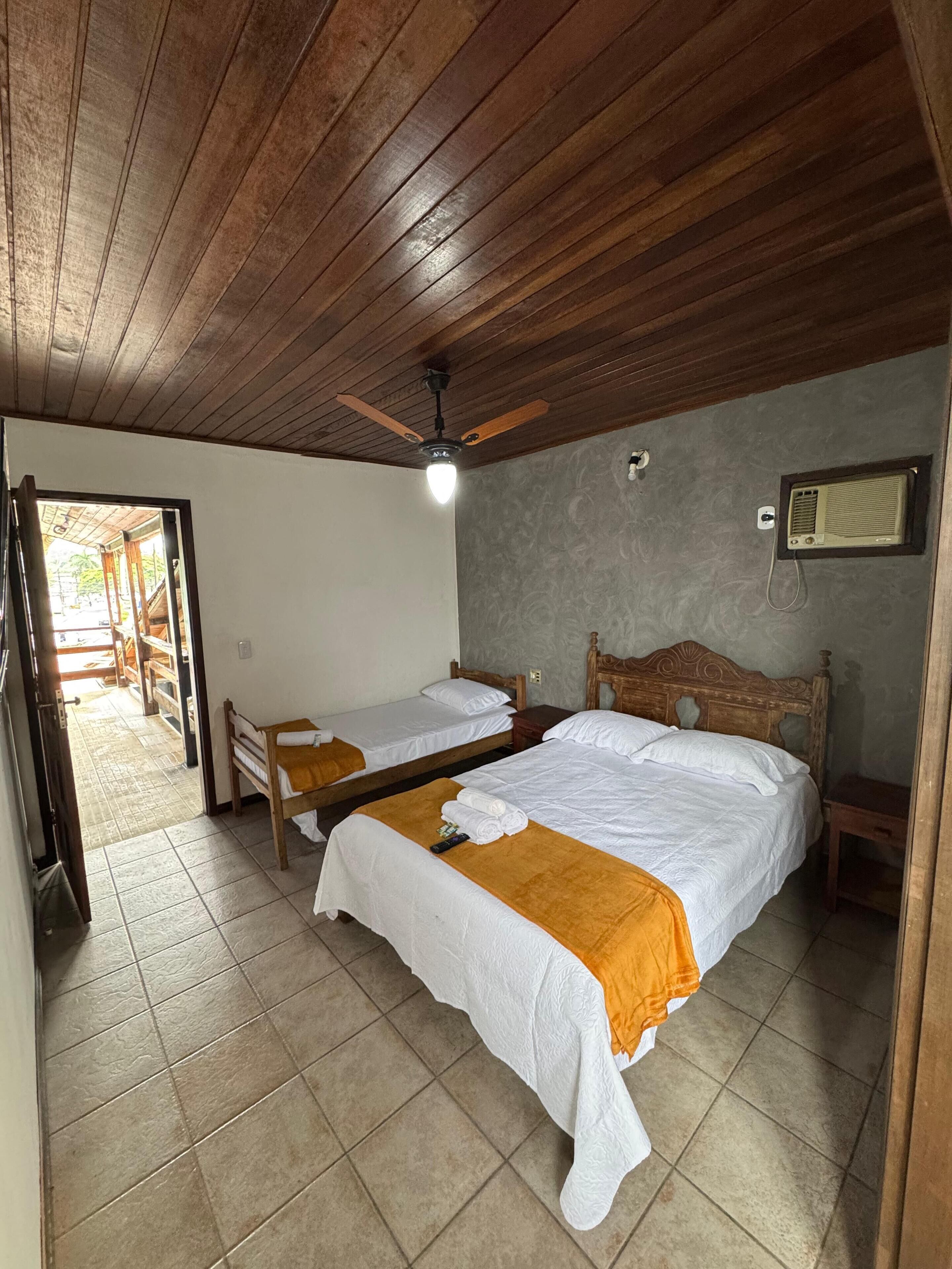A room with two beds, wooden ceiling, and a ceiling fan.