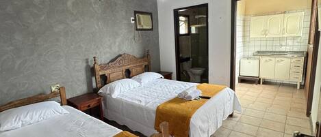 Ein Zimmer mit zwei Holzbett, einem Deckenventilator, einem kleinen Tisch und einem durchgehenden Türspalt sichtbaren Badezimmer.