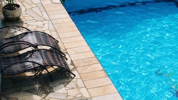Una piscina con sillas de descanso y una mesa, rodeada de baldosas de piedra y un mural.